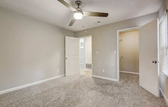 an empty living room with a ceiling fan and a door to a bathroom