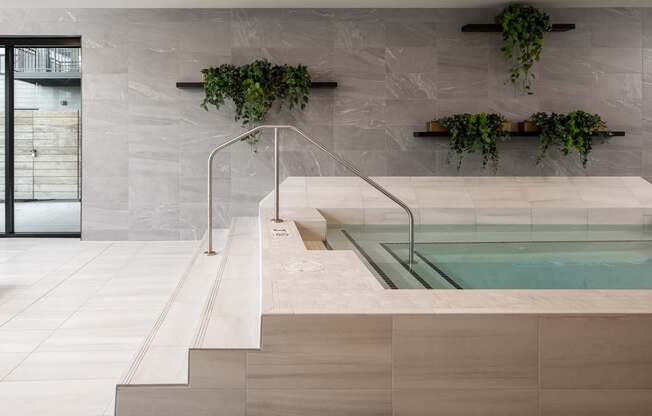 A modern indoor swimming pool with a glass enclosure and a wooden ledge.