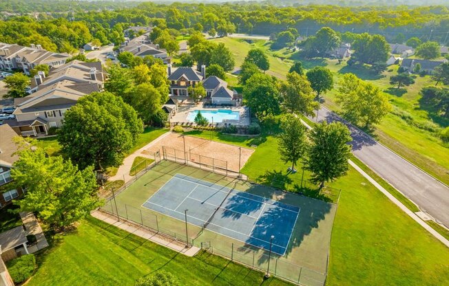 an aerial view of a house with a tennis court in the foreground and a swimming pool in