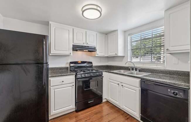 A black refrigerator is in a kitchen with white cabinets.