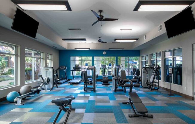 a gym with cardio equipment in a large room with windows