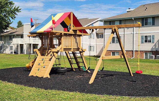 A wooden swing set with a red ball on the ground.