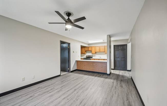 an empty living room with a ceiling fan and a kitchen