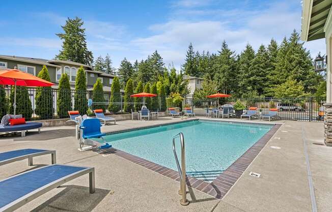 A pool with a red umbrella and blue chairs.