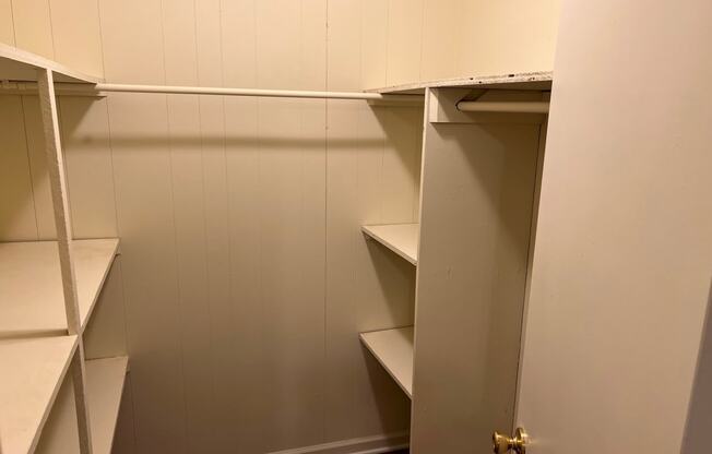 a walk in closet with white shelves and a door