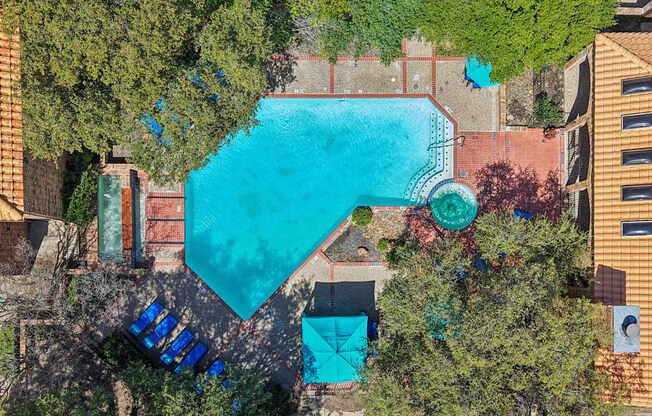 An aerial view of a swimming pool surrounded by trees and buildings.