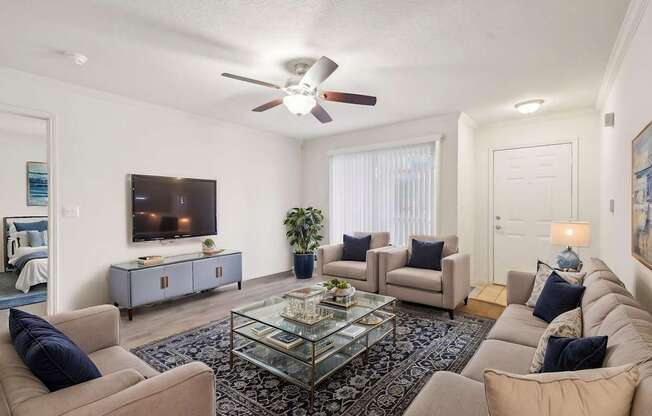A living room with a glass coffee table and a television on the wall.