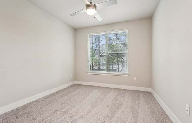 A spacious bedroom with a ceiling fan and a window overlooking  trees.
