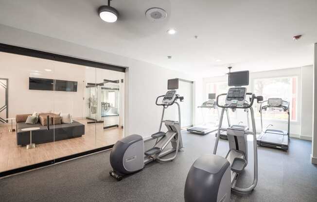 the gym is equipped with cardio equipment and a large mirror