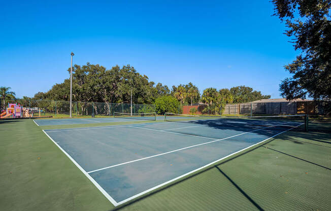 A tennis court surrounded by trees and a fence.