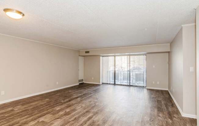 A spacious room with wooden flooring and a sliding glass door.