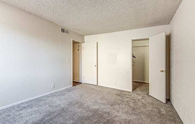 A room with carpeted floor and white walls with three doors.