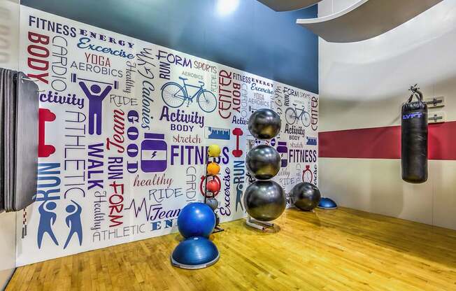 A gym with a wall covered in fitness related words and a row of exercise balls.