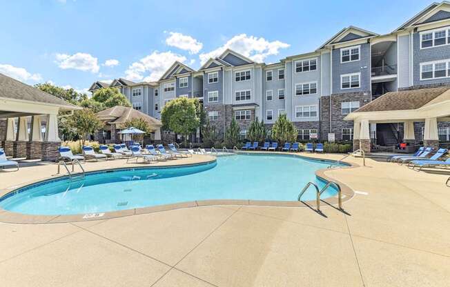A large swimming pool surrounded by apartment buildings and lounge chairs.