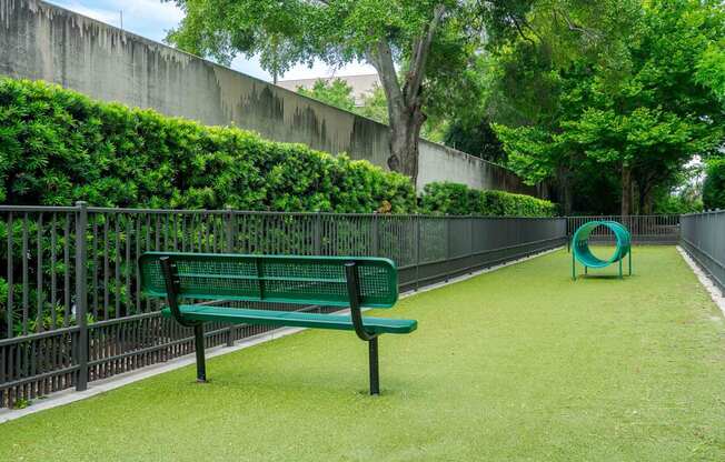 A green bench sits on a green lawn next to a green playground equipment.