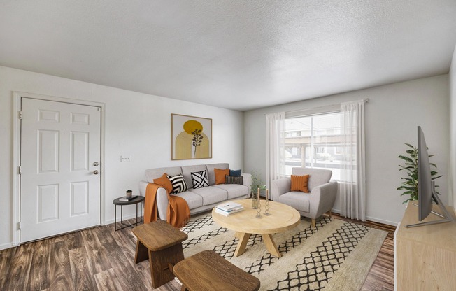 Apartments for Rent in West Las Vegas - Portola Del Sol - Living Room Area with Neutral Color Couch, Large Circle Coffee Table, Short Round Stools, Wood-Style Flooring, and a Large Window