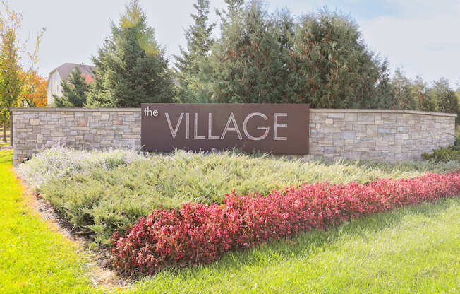 a sign for the village on a stone wall with flowers