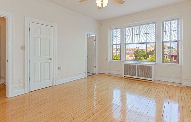 an empty living room with a ceiling fan, hardwood floors and three windows at the calverton apartments in washington dc