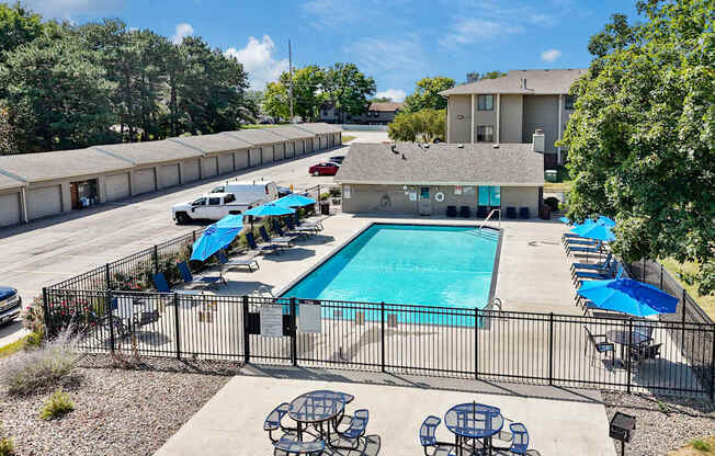 A pool surrounded by a black fence with blue umbrellas and chairs.
