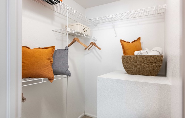 a walk in closet with pillows and a basket on a shelf in a closet