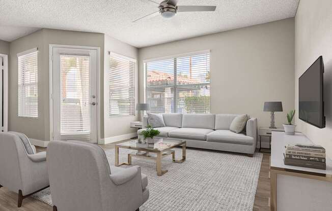 A living room with a grey sofa, two grey armchairs, a coffee table, and a flat-screen TV mounted on the wall.