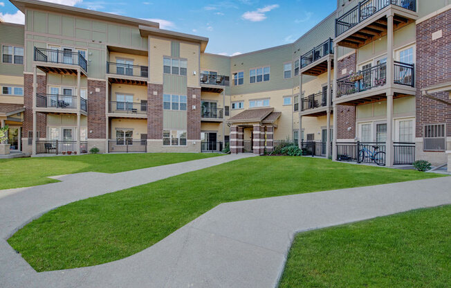 A welcoming exterior courtyard here at Swan Creek with manicured green lawn, modern building facades, private balconies, and walking paths, creating a bright, inviting, and well-maintained community setting.
