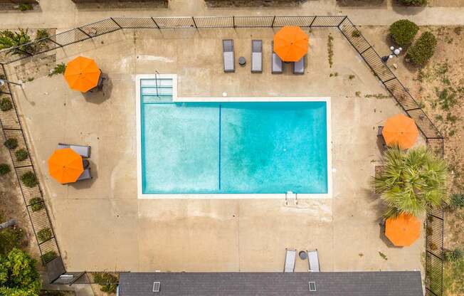 An aerial view of a swimming pool surrounded by orange umbrellas and lounge chairs.