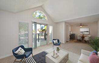 a living room with blue chairs and a white coffee table and a sliding glass door to the private balcony.   Extra rounded windows above the patio door which allow more natural light in.