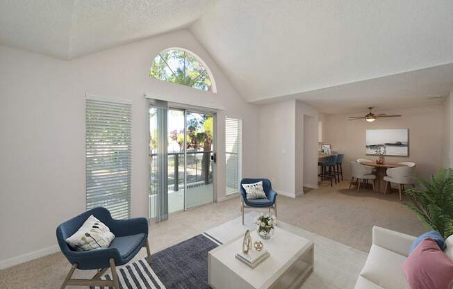 a living room with blue chairs and a white coffee table and a sliding glass door to the private balcony.   Extra rounded windows above the patio door which allow more natural light in.