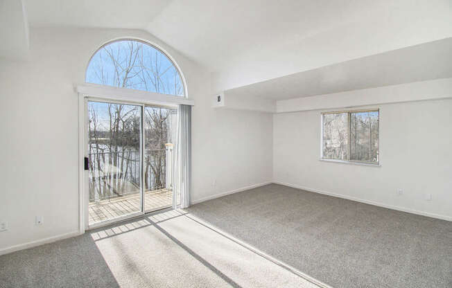 A living room with a cathedral ceiling, large arched window and a slider to a balcony at West Hampton Park Apartments in Elkhorn, NE 68022