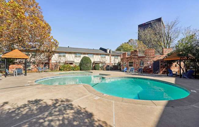A large outdoor swimming pool surrounded by a patio area with chairs and a gazebo.