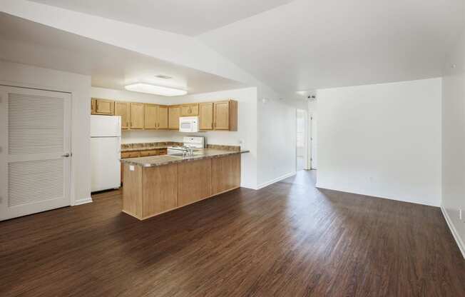 an empty living room and kitchen with wood floors and white walls