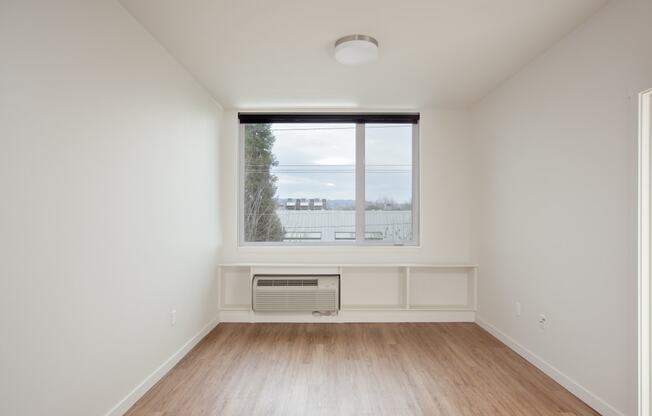 an empty living room with a large window and wooden floors