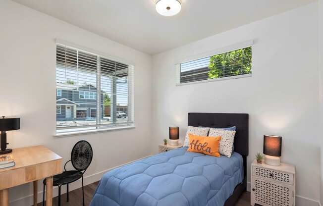 a bedroom with a bed and a desk and two windows