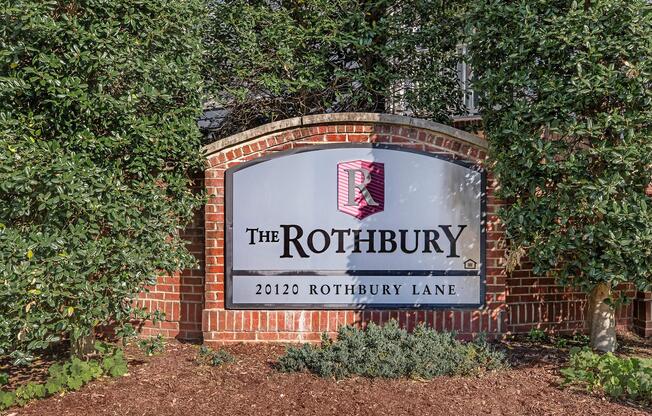 Sign for "The Rothbury" located at 20120 Rothbury Lane. The sign is set against a brick background, surrounded by greenery and landscaping.