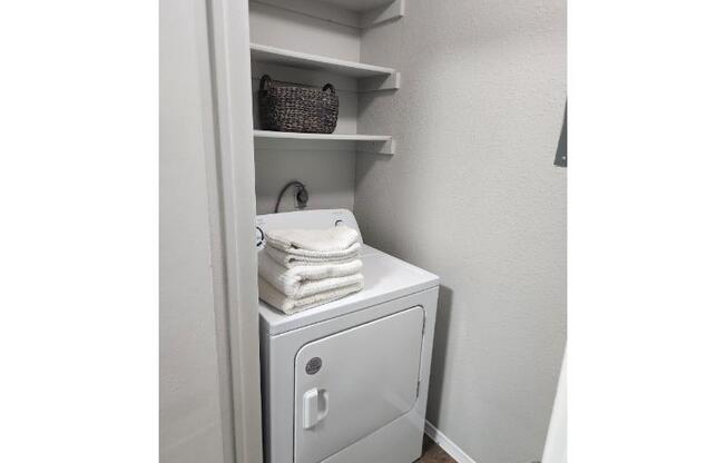A white laundry machine is in a cabinet with towels on top.