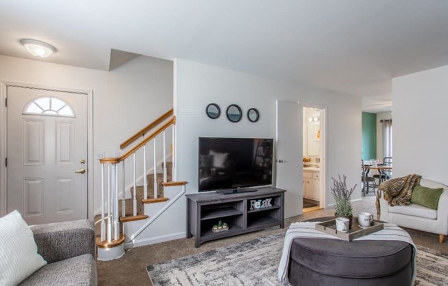 Model unit living room with a staircase in the background and a couch and chair in the foreground.