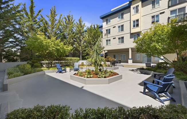 a courtyard with a large tree in the center and a seating areas with blue Adirondack chairs at Guinevere Apartment Homes, Seattle