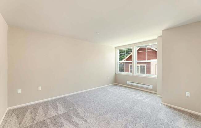 A room with a carpeted floor and a window showing a red building outside.