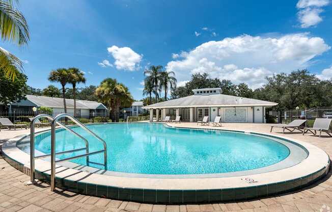 a swimming pool with chairs and a building in the background at Aqua Bay Apartments in Naples, FL 34116