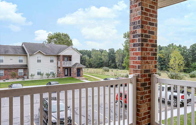 A white house with a brick pillar in front of a parking lot.