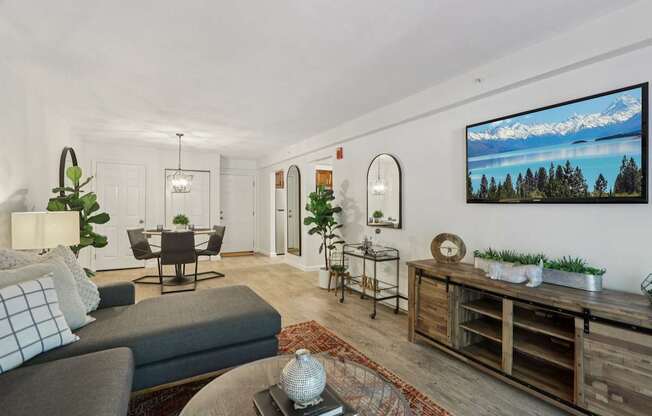 A modern living room with a grey sofa, a wooden cabinet, and a large TV mounted on the wall.