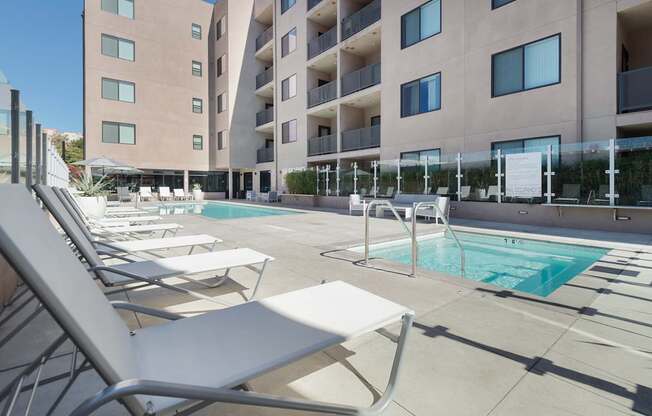 A pool area with sun loungers and a building in the background.