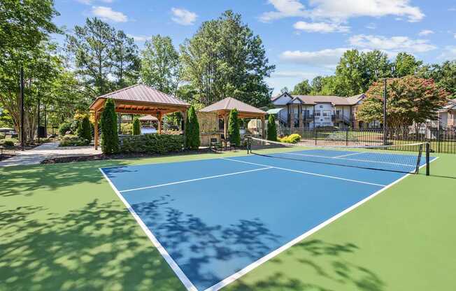 A tennis court is surrounded by trees and a gazebo.