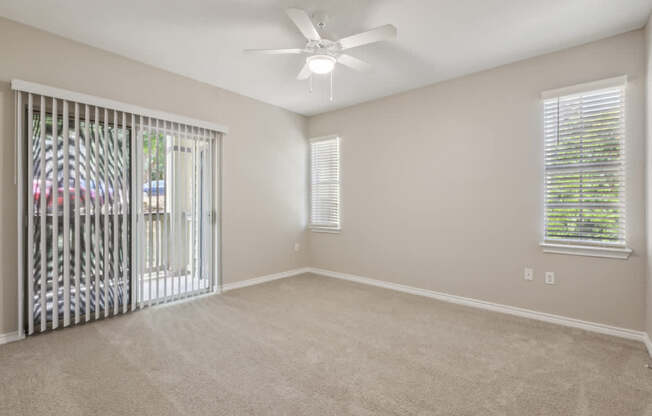 A room with a fan, carpeted floor, and a window with blinds.