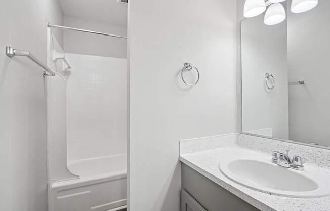 A white bathroom with a sink, mirror, and shower.