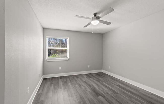 A room with a ceiling fan and a window with a view of trees.