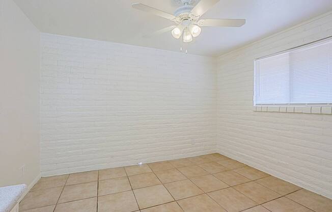 A room with a ceiling fan and a window with blinds.