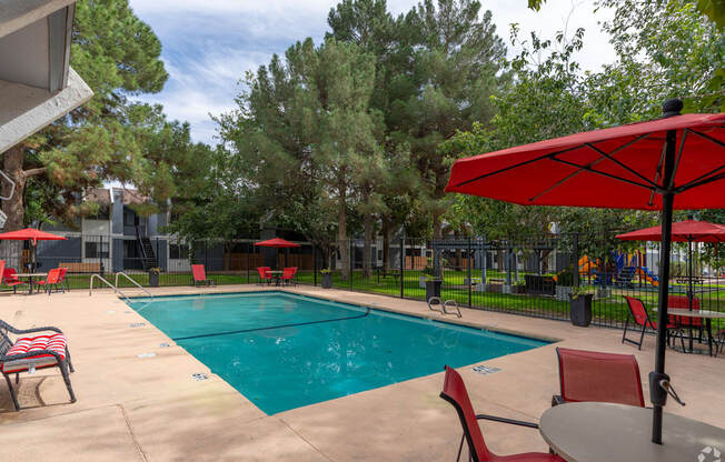 A pool area with red chairs and umbrellas.