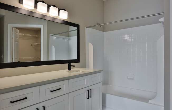 A bathroom with a white tub and a large mirror above the sink.